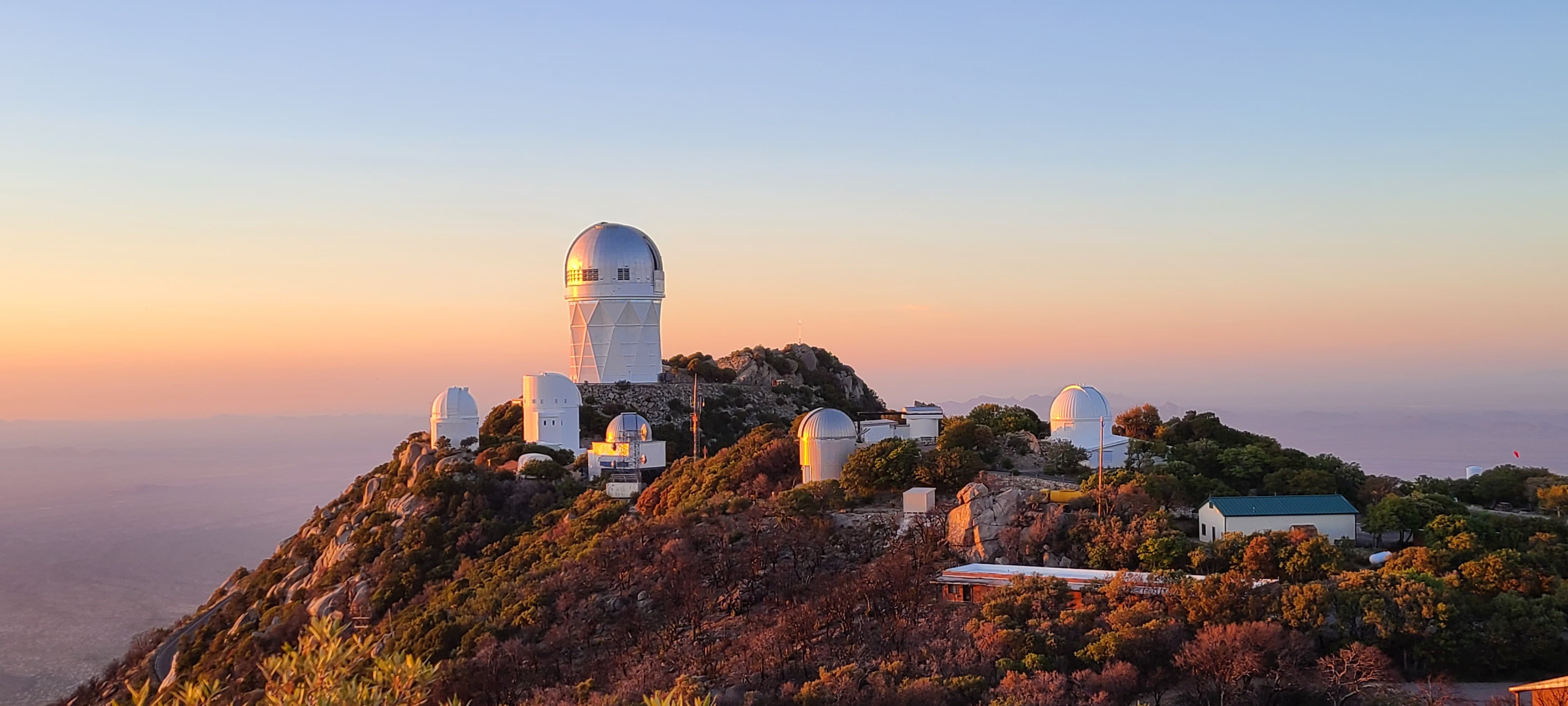 A mountain peak filled with trees and many white domes against a sunset sky.